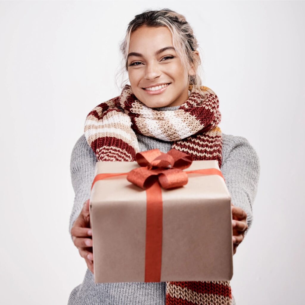 Studio portrait of an attractive young woman handing you a gift while dressed in Christmas-themed attire