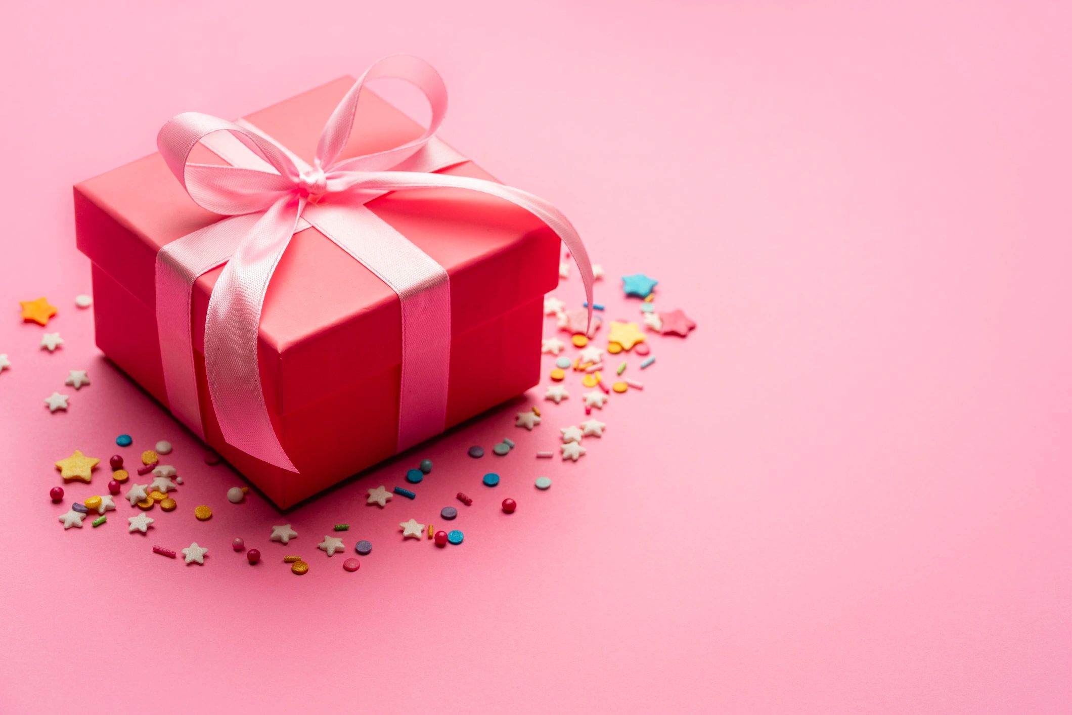 Pink birthday gift box with ribbon and confetti